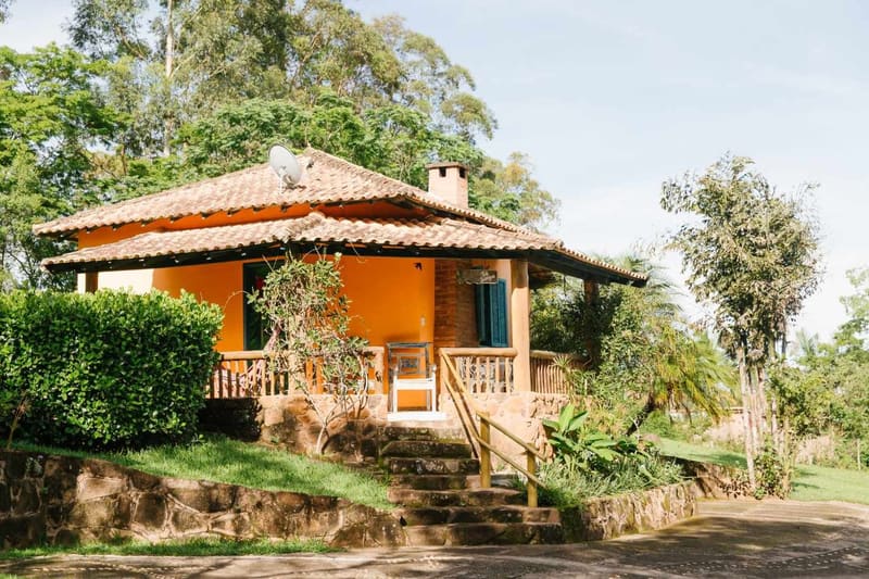 Chalé laranja com varanda de madeira entre jardins