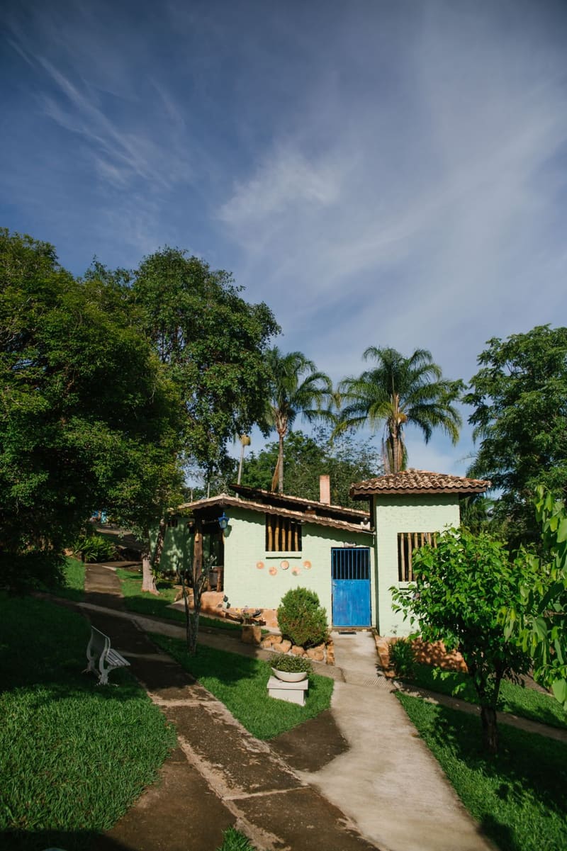 Caminho entre árvores até um chalé branco de portas azuis